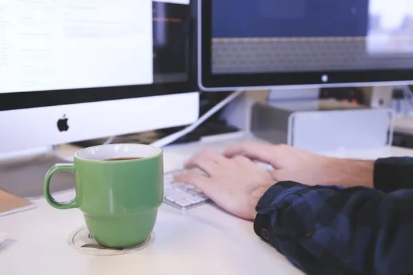 Hands typing on a keyboard next to a green coffee mug